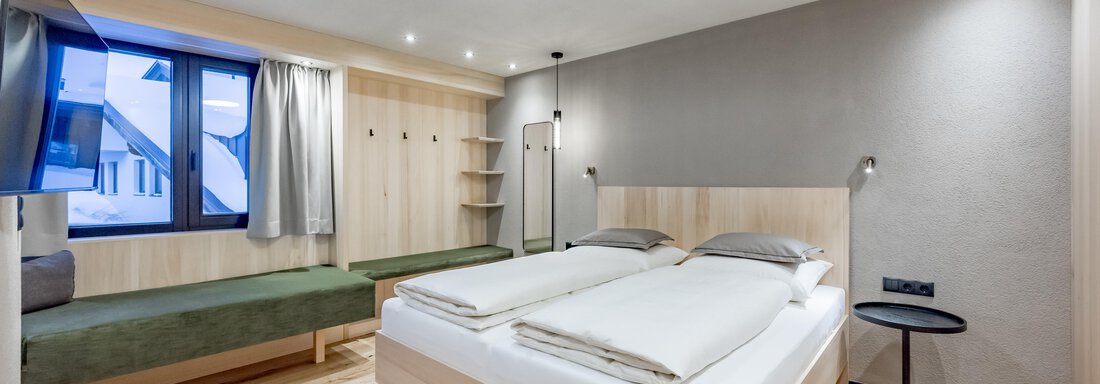 A modern bedroom with bright wood design and large windows. The room features a double bed and a cozy seating area. - Hotel-Garni Pirchhütt - Obergurgl 