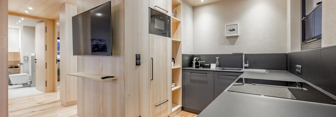 A modern kitchen with light wooden elements and dark worktops. It is well-lit and contains contemporary appliances. - Hotel-Garni Pirchhütt - Obergurgl 