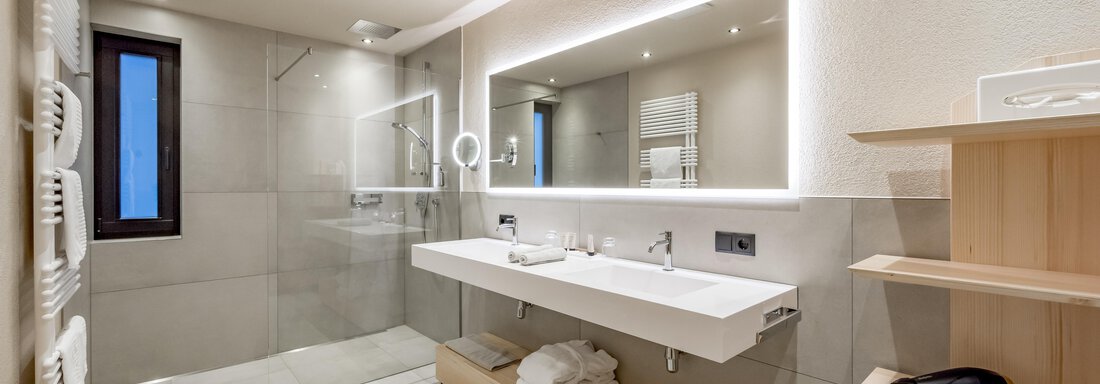 A modern bathroom with stylish design. It features a sink, a large mirror, and a walk-in shower. - Hotel-Garni Pirchhütt - Obergurgl 