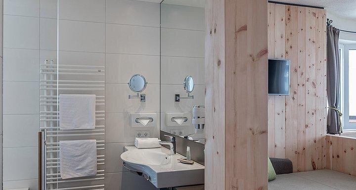 A modern bathroom with a shower and a sink. The walls are partly made of wood and there is a television in the room. - Hotel-Garni Pirchhütt - Obergurgl 