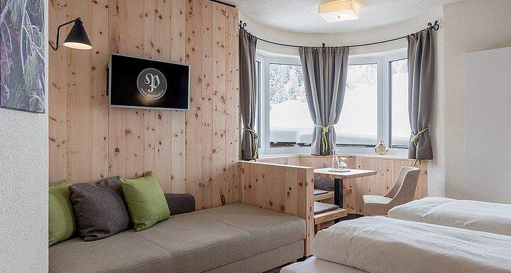 A modern hotel room with wooden paneling and large windows. There is a cozy seating area, a table, and two single beds. - Hotel-Garni Pirchhütt - Obergurgl 