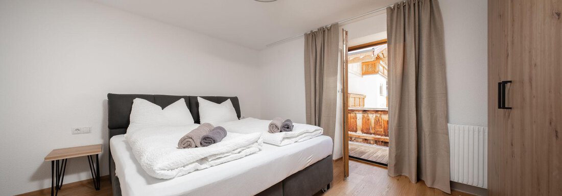 A cozy bedroom with a double bed and wooden flooring. The large windows provide access to a balcony and plenty of daylight. - Mountain Lodge Obergurgl - Obergurgl 