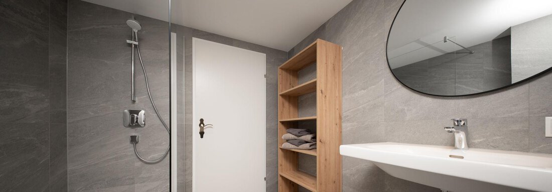 A modern bathroom with a rain shower and a washbasin.  
Wooden shelves hold fresh towels. - Mountain Lodge Obergurgl - Obergurgl 