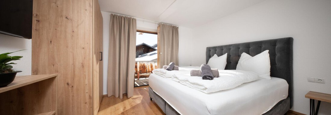 A modern hotel room with a large bed and wooden furniture. The room has access to a balcony with a view. - Mountain Lodge Obergurgl - Obergurgl 