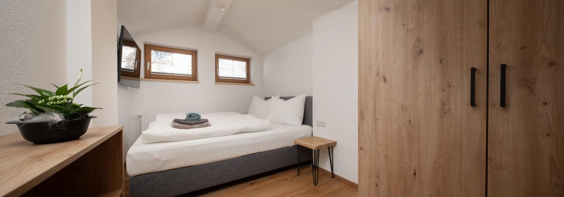 A cozy room with a double bed and bright windows. A wooden shelf and wardrobe complement the modern decor. - Mountain Lodge Obergurgl - Obergurgl 