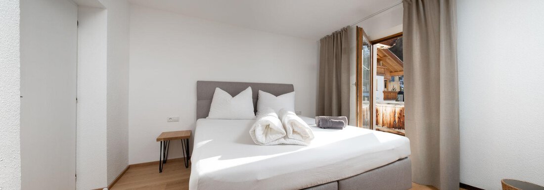 A bright bedroom with a large bed and wooden floor. The windows are open and let in daylight. - Mountain Lodge Obergurgl - Obergurgl 