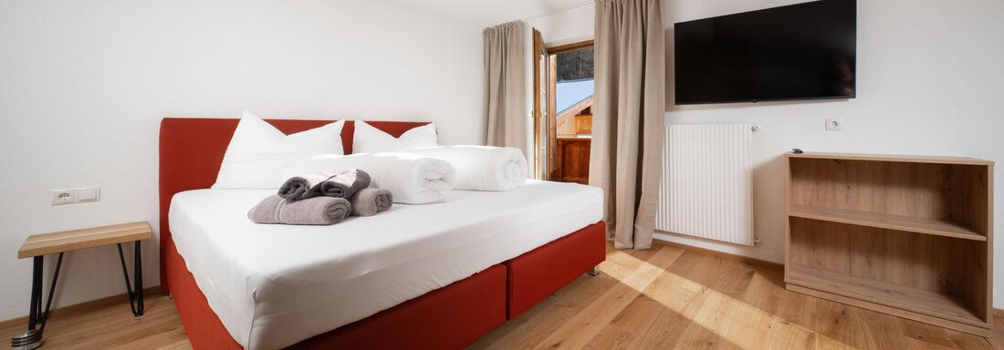 A modern bedroom with a red bed and bright walls. The room has large windows and a cozy atmosphere. - Mountain Lodge Obergurgl - Obergurgl 