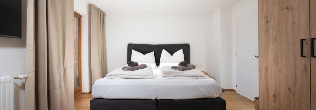 A modern bedroom with a large bed and elegant bedding. The warm wooden floors and simple style create an inviting atmosphere. - Mountain Lodge Obergurgl - Obergurgl 