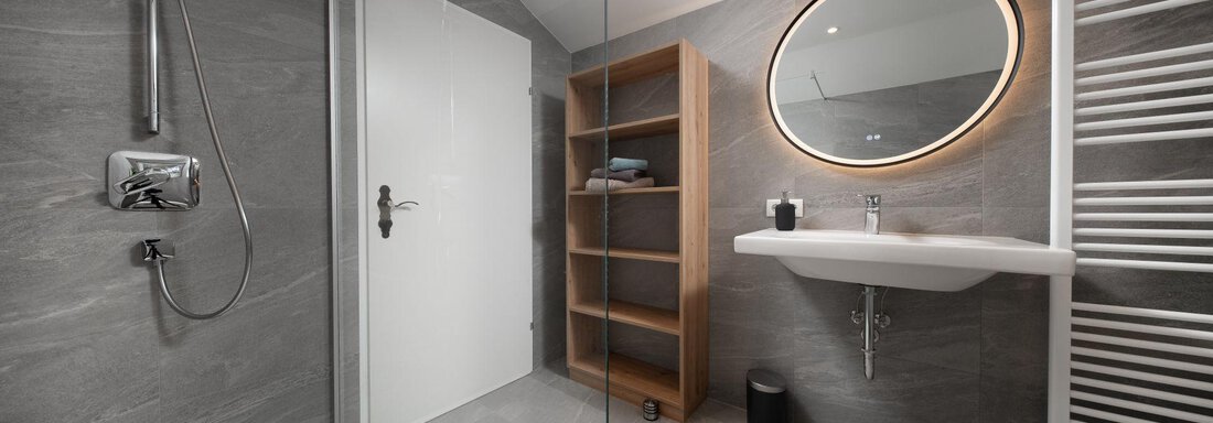 A modern bathroom with gray tiles and round mirror lighting. The shower and the towel holder are also clearly visible. - Mountain Lodge Obergurgl - Obergurgl 