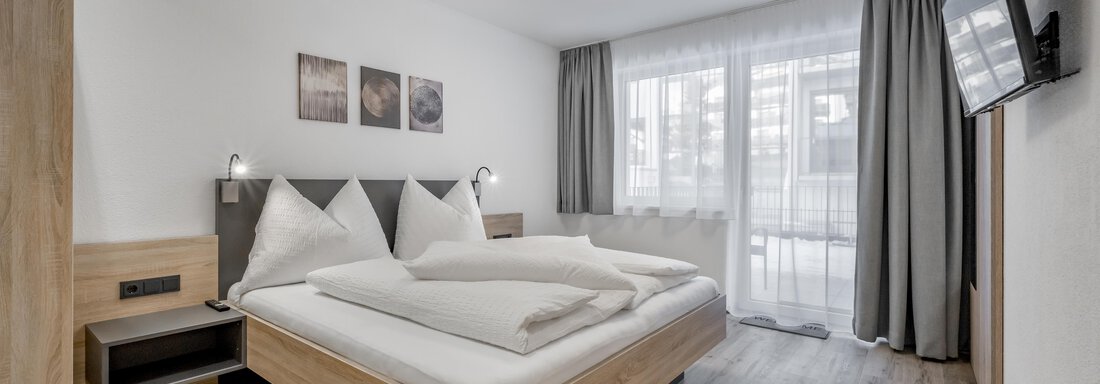 A modern bedroom with a double bed and two large cushions. The room has a bright atmosphere with a window and a television. - Peak Gurgl - Obergurgl 