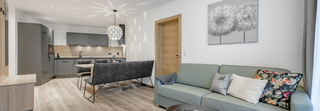 A modern living room with a gray sofa and a round table. The open kitchen in the background creates a bright and inviting atmosphere. - Peak Gurgl - Obergurgl 