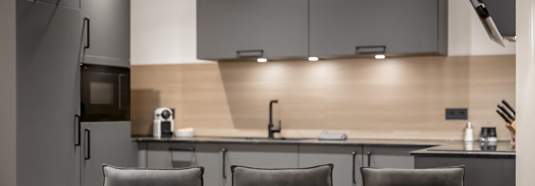 A modern kitchen with gray cabinets and light wood surfaces.  
The dining area is simple and elegant, with a stylish table and comfortable chairs. - Peak Gurgl - Obergurgl 