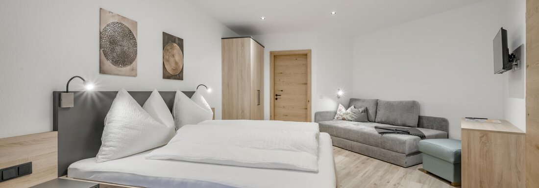 A modern room with a double bed and a cozy couch. There are light walls, wooden flooring, and a contemporary decor. - Peak Gurgl - Obergurgl 