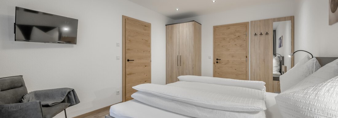A modern bedroom with a double bed and a television on the wall. Bright walls and wooden doors create an inviting atmosphere. - Peak Gurgl - Obergurgl 