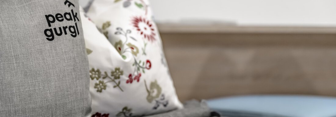 A stylish sofa with decorative cushions. One of the cushions has the inscription "peak gurgi" and a gray cloth is lying next to it. - Peak Gurgl - Obergurgl 
