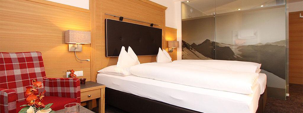 Ein modernes Hotelzimmer mit einem Doppelbett und einer gemütlichen Sitzecke. Auf dem Tisch stehen frisches Obst und Getränke. - Pension Hohenfels - Obergurgl 