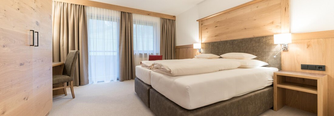 Ein modernes Schlafzimmer mit zwei Betten und einem gemütlichen Holzdesign. Große Fenster sorgen für viel natürliches Licht und einen einladenden Raum. - Pension Hohenfels - Obergurgl 
