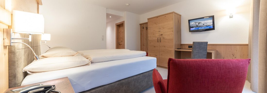 Ein gemütliches Hotelzimmer mit einem Doppelbett und einem roten Stuhl. Der Raum ist modern und hell, mit einem Fernseher und einer Schreibtischecke. - Pension Hohenfels - Obergurgl 