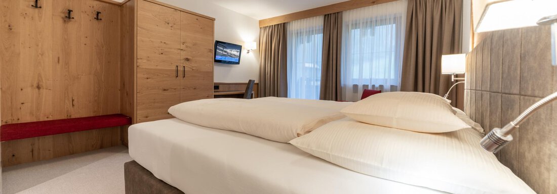 Ein gemütliches Hotelzimmer mit einem Doppelbett und einem Holzkleiderschrank. Die großen Fenster lassen viel Tageslicht herein. - Pension Hohenfels - Obergurgl 