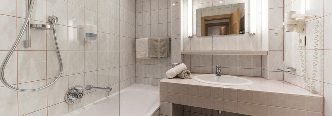 Ein modernes Badezimmer mit einer Badewanne und einer Dusche. Es ist hell und mit Fliesen in neutralen Farbtönen ausgestattet. - Pension Hohenfels - Obergurgl 
