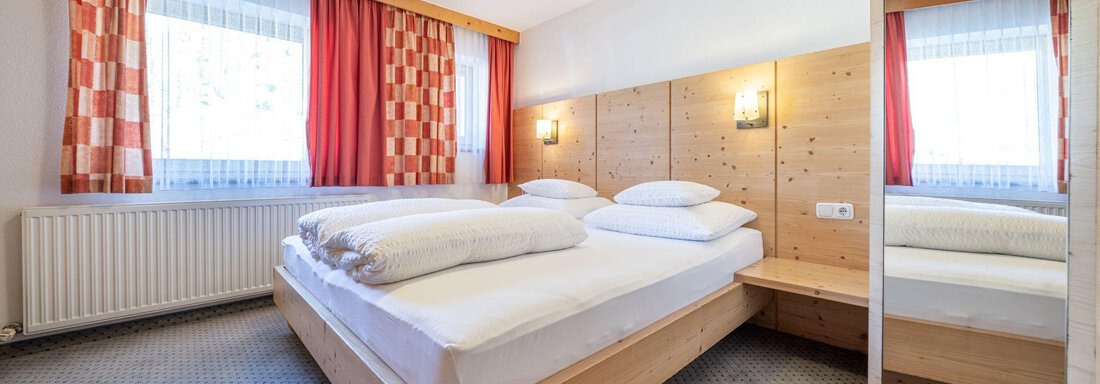 A cozy bedroom with a wooden bed and large windows. The walls are light, and there are curtains in warm colors. - Schönblick Gurgl - Obergurgl 