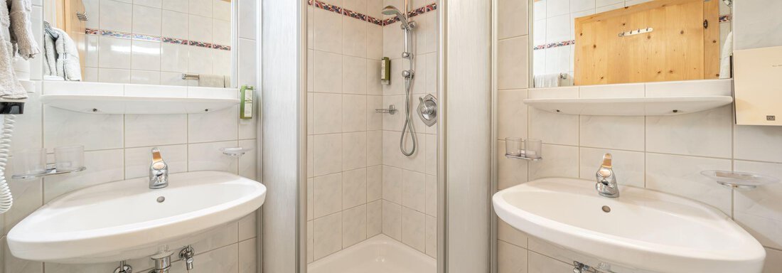 A bright bathroom with two sinks and a shower. The walls are tiled, and wooden ceilings create a warm atmosphere. - Schönblick Gurgl - Obergurgl 