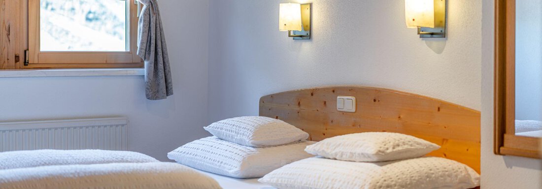 A cozy bedroom with a double bed and several pillows. The room has light-colored walls and a window with a beautiful view. - Schönblick Gurgl - Obergurgl 