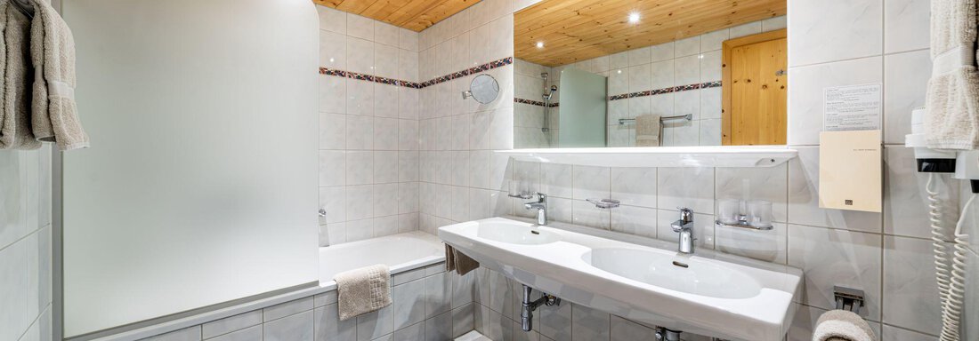 A modern bathroom with a bathtub and a shower. The floor is designed with blue and white tiles and there is large mirror lighting. - Schönblick Gurgl - Obergurgl 