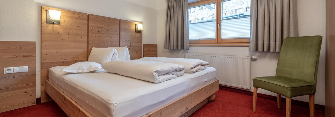 A cozy bedroom with a double bed and a chair. Large windows let in daylight and the walls are painted in warm colors. - Schönblick Gurgl - Obergurgl 