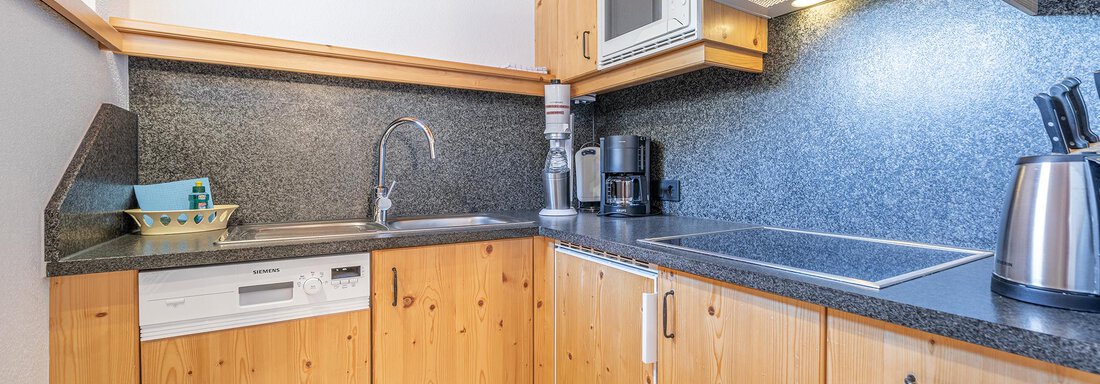 A modern kitchen with wooden cabinets and a dark countertop. It is equipped with basic appliances such as a stove, a microwave, and a dishwasher. - Schönblick Gurgl - Obergurgl 