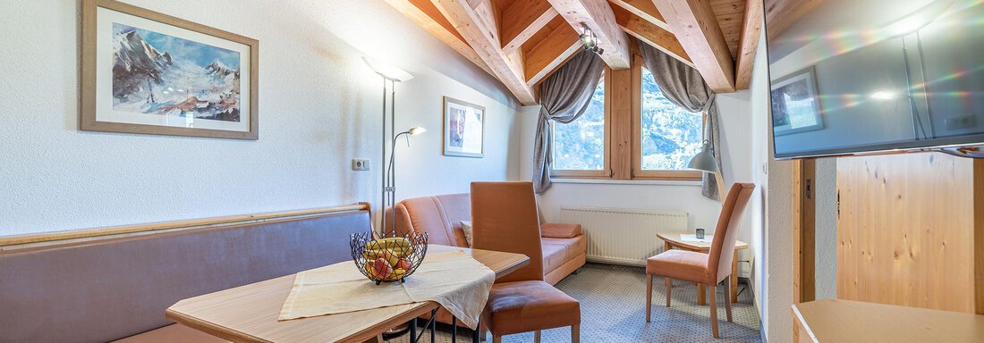 Wohnraum Appartement "1" A cozy living area with a wooden ceiling and modern furniture. A table, chairs, and a television are available, with a window that lets in plenty of light. - Schönblick Gurgl - Obergurgl