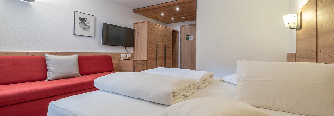 A cozy room with a large bed and additional pillows. It also features a red sofa and modern amenities like a television. - Schönblick Gurgl - Obergurgl 
