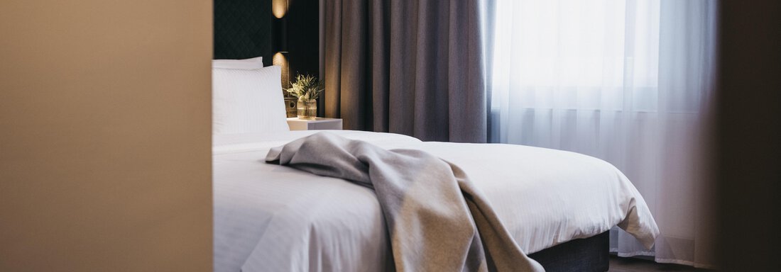 A modern bedroom with a bed and elegant curtains. A blanket lies on the bed, and the light softly filters through the window. - The Crystal VAYA Unique - Obergurgl 