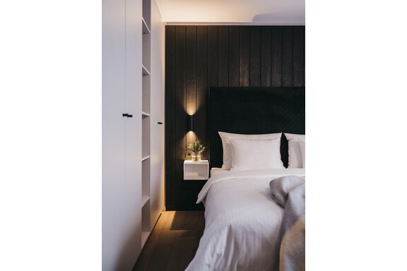 A modern bedroom with a large, comfortable bed and soft lighting. The walls are in dark tones and an elegant white dresser stands next to it. - The Crystal VAYA Unique - Obergurgl 