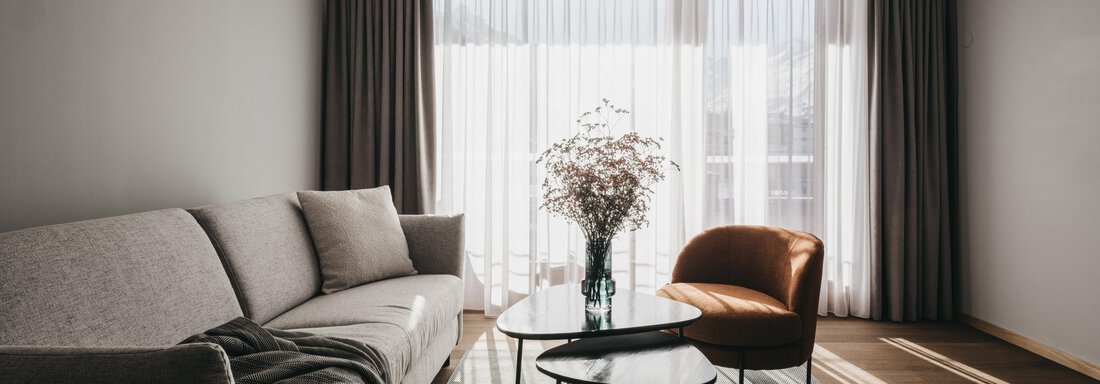 A modern living room with a grey sofa and a cozy armchair. Large windows let in plenty of daylight, and decorative plants create a pleasant atmosphere. - The Crystal VAYA Unique - Obergurgl 