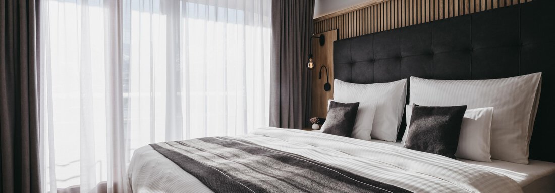 A modern bedroom with a large bed and elegant furnishings. Large windows let in plenty of daylight. - The Crystal VAYA Unique - Obergurgl 