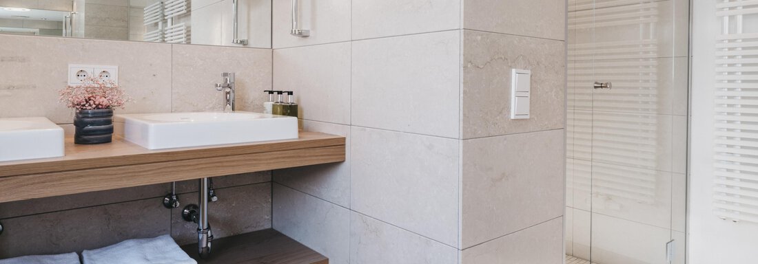 A modern bathroom with an elegant wooden sink shelf and a large mirror. The shower is separated by glass walls, and the light gently filters in. - The Crystal VAYA Unique - Obergurgl 