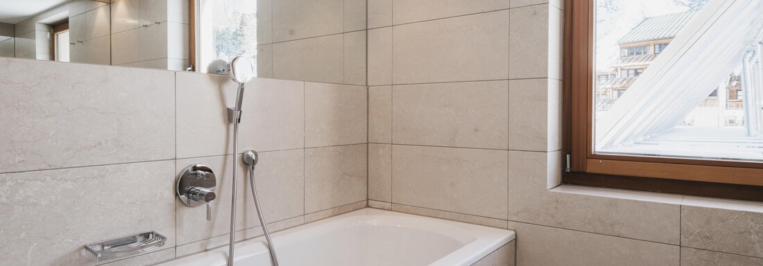 A modern bathroom with a bathtub and a window. The walls are clad with light tiles that create an inviting atmosphere. - The Crystal VAYA Unique - Obergurgl 