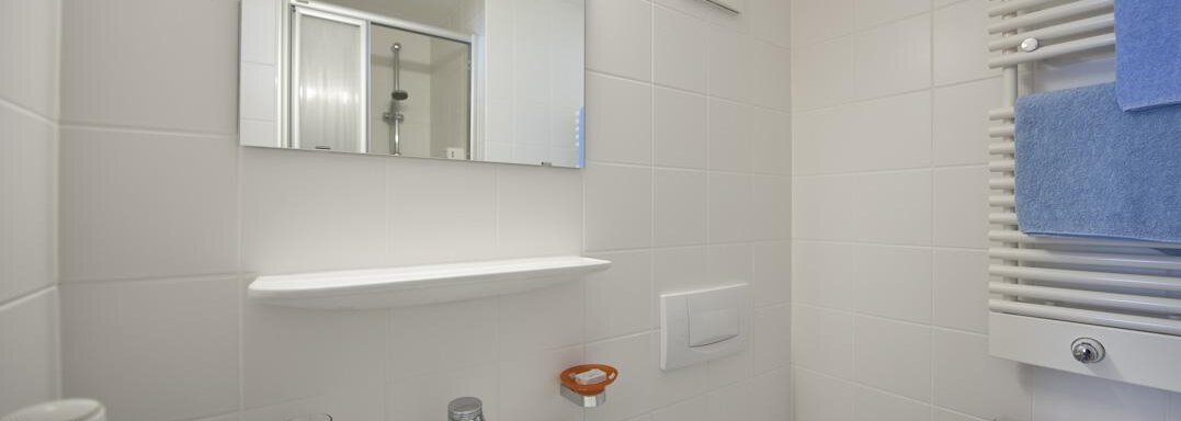 A modern bathroom with a sink, a mirror, and white tiles. Towels in blue and a shower in the background complete the furnishings. - Universitätszentrum Obergurgl - Obergurgl 