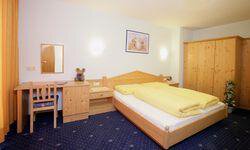Ein einfaches Zimmer mit einem Bett und gelben Bettdecken. Es gibt einen Tisch, einen Stuhl und einen Kleiderschrank aus Holz. - Appartement Haus König - Obergurgl 