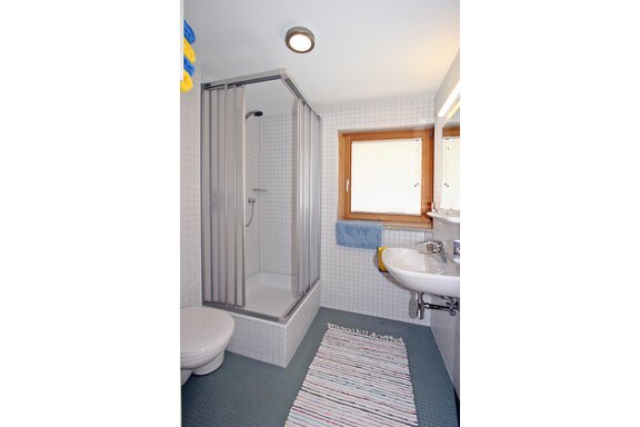 A modern bathroom with a shower and a sink. The walls are tiled, and there is a large window that lets in daylight. - Ferienwohnungen Broser - Obergurgl 