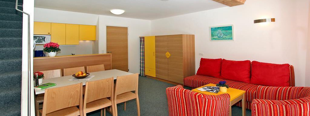 Wohnküche A bright and modern living kitchen with red sofas and a wooden dining area. The walls are in neutral tones, and there are colorful accents from decorations and furniture. - Ferienwohnungen Broser - Obergurgl