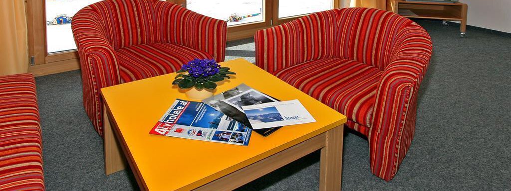 A cozy seating area with two red-striped armchairs and a yellow table. On the table are brochures and a small decoration. - Ferienwohnungen Broser - Obergurgl 