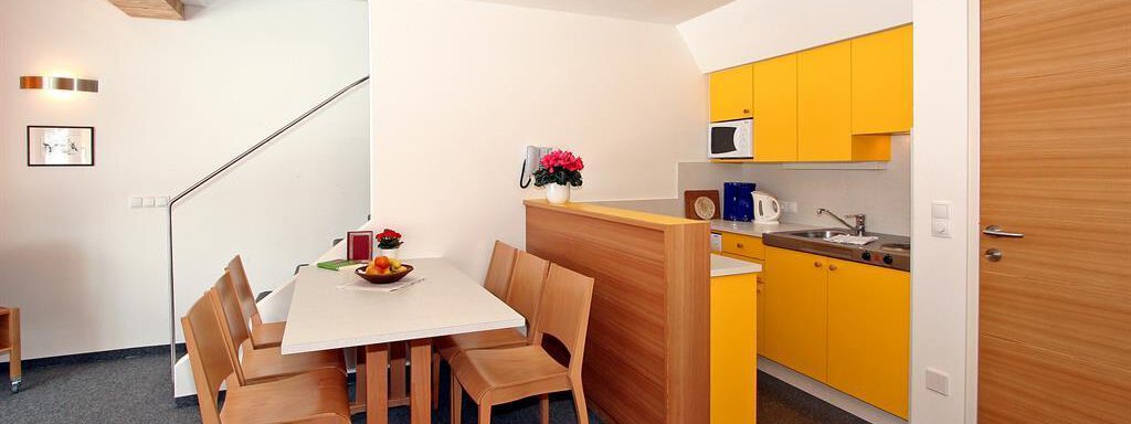 A bright and modern kitchen with yellow cabinets and a dining table. The room is designed to be friendly and inviting. - Ferienwohnungen Broser - Obergurgl 