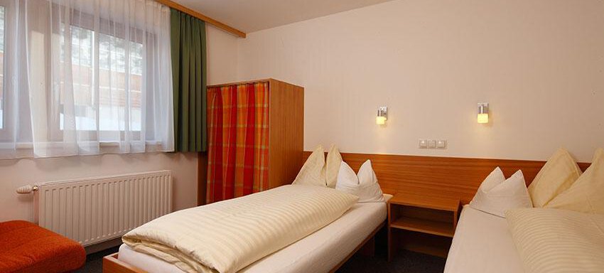A cozy bedroom with two single beds, a sofa, and a large window. The walls are in neutral tones, and there are decorative cushions. - Ferienwohnungen Broser - Obergurgl 