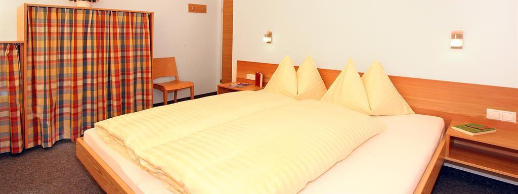 A cozy hotel room with a large double bed and two pillows. There is a wardrobe and some wooden furniture. - Ferienwohnungen Broser - Obergurgl 