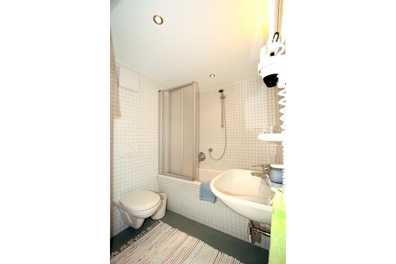 A modern bathroom with a bathtub, shower, and sink. White tiles and a bright, inviting space create a pleasant atmosphere. - Ferienwohnungen Broser - Obergurgl 