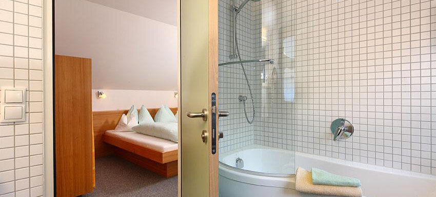 A modern bathroom with a bathtub and a shower. In the background, a cozy sleeping area is visible. - Ferienwohnungen Broser - Obergurgl 
