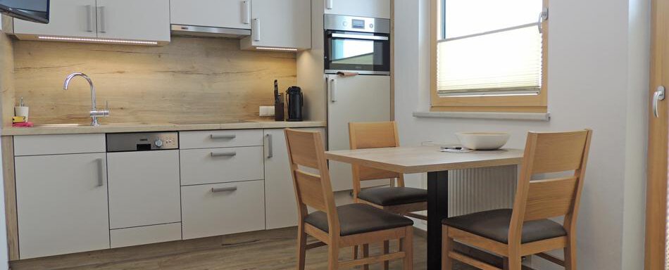 A modern kitchen with bright cabinets and a small dining table. The room is well-lit and furnished in a friendly manner. - Haus Christophorus - Obergurgl 