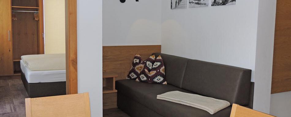 A cozy room with a sofa and a dining table. In the background, there is a bed and some decorative pictures on the wall. - Haus Christophorus - Obergurgl 